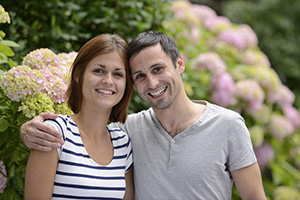 Couple posing outside next to a brush of flowers