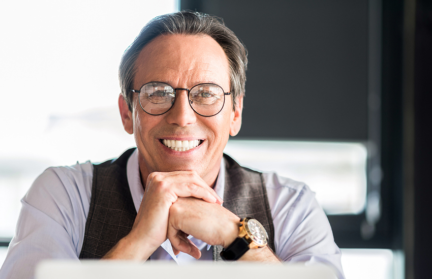 Pleasant mature businessman sitting at table with smile