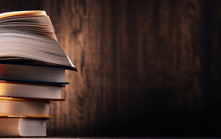 A thick stack of books sitting on a table. The top book is open wide as if someone was currently reading it.