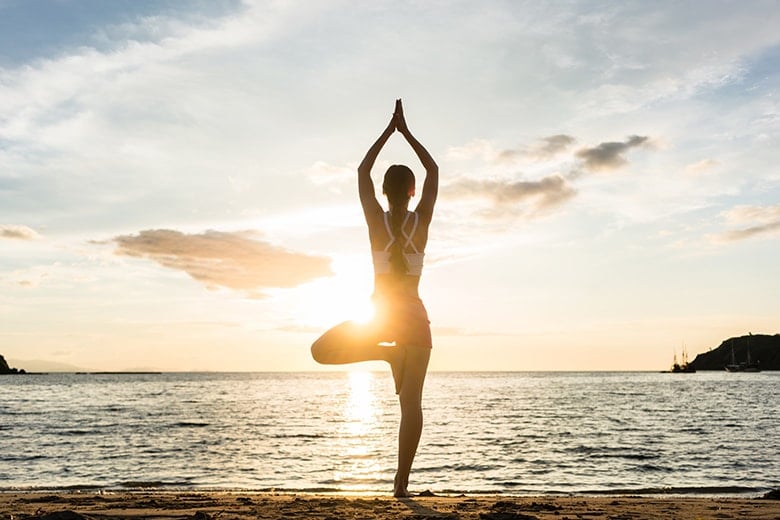 A woman does a yoga pose on the beach, like the one on Hilton Head Island. She understands how yoga helps her focus and challenges her nerves and muscles. 
