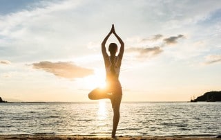 A woman does a yoga pose on the beach, like the one on Hilton Head Island. She understands how yoga helps her focus and challenges her nerves and muscles.