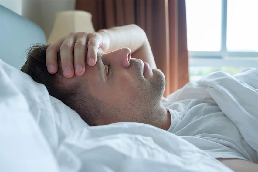 man suffering from a morning headache, laying in bed